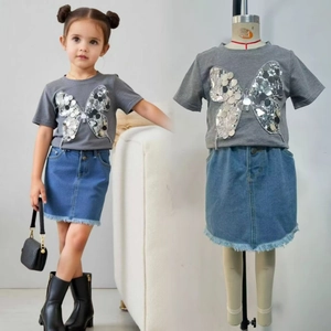 Détail du t-shirt gris à papillon en sequins et jupe en jean avec ourlet effiloché