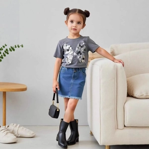 Détail d'un t-shirt gris à papillon pailleté et d'une jupe en jean effilochée pour fille