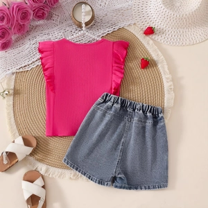 Flat lay of girls strawberry denim shorts and pink ruffled top on a woven mat