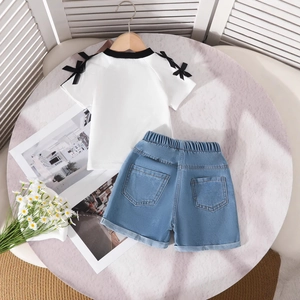 Detail eines Mädchen-Baumwolltops mit schwarzen Schleifen und blauen Denim-Shorts