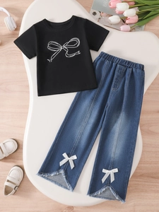 Girls' black t-shirt with bow print and blue denim wide-leg pants set on wooden desk