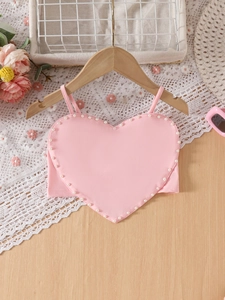 Pink heart-shaped girls vest with bead trim on a wood background with flowers