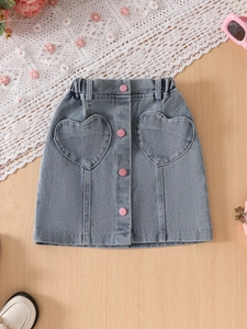 Girls denim skirt with heart pockets and pink buttons on light wooden background