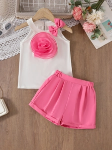 Girls summer two-piece set with white floral lace top and pink shorts on wooden background