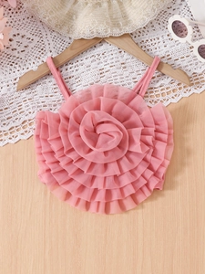Pink mesh tank top with a large 3D flower applique on a wooden hanger with summer props