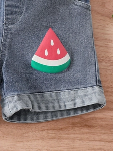 Close-up of girls denim shorts featuring a cute watermelon patch and rolled hem design