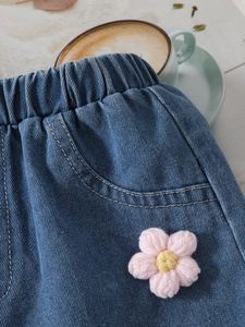 Detail view of denim shorts with elastic waist and a pink handmade crochet flower
