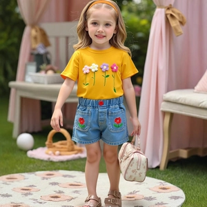 Detail of girls yellow t-shirt with floral appliques and denim shorts on child model