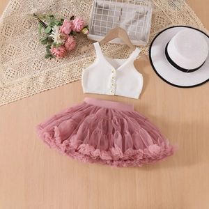 Dettaglio del gilet bianco in maglia per neonata con bottone a fiore e gonna di tulle rosa