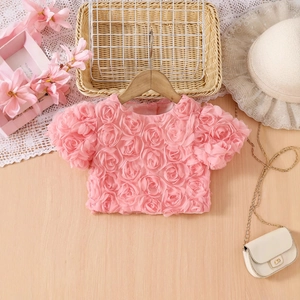 Détail d'un haut rose pour fille orné de fleurs de roses 3D et d'une texture luxueuse