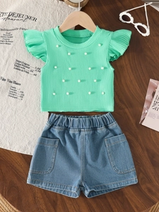 Detailed view of mint green ribbed top with white pearls and denim shorts set on wood