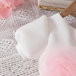 Détail d'une fleur 3D en gaze rose sur une robe de princesse blanche pour fille