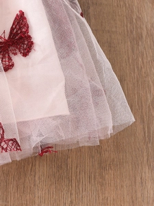 Rosa Tüllkleid für Mädchen mit roten Schmetterlingsstickereien auf einem Holzgrund