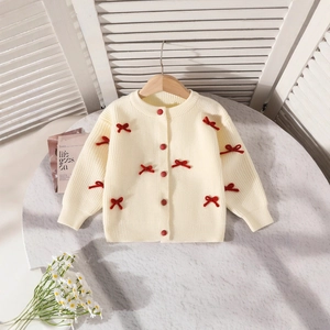 Détail du cardigan en maille avec nœuds rouges et boutons sur un cintre en bois