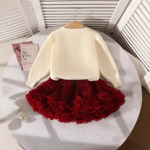 Détail d'un pull en maille crème pour filles et d'une jupe tutu rouge sur marbre