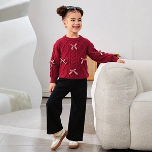 Close-up of red cable knit sweater with bow accents and black corduroy pants set