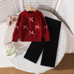 Detail of red cable-knit girls' sweater with gingham bows and black ribbed pants