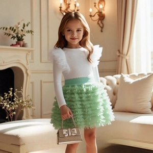 Close-up of white knitted top with ruffled tulle shoulders and mint green tutu skirt