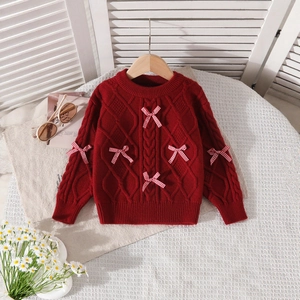 Detailed close-up of red cable knit sweater featuring festive checkered bow accents