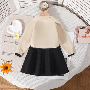 Détail de la robe tricotée pour enfant avec haut crème et jupe plissée noire sur cintre
