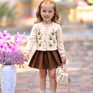 Dettaglio del cardigan ricamato e del set gonna a pieghe in maglia per bambine