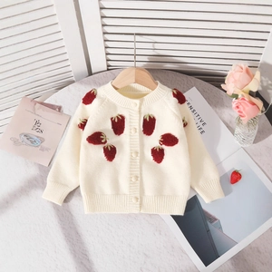 Détail d'un cardigan tricoté pour bébé avec broderie fraise rouge sur tissu crème