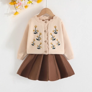 Dettaglio cardigan beige per bambina con ricami floreali e gonna a pieghe marrone