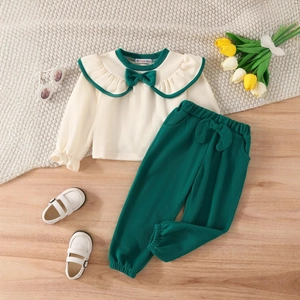 Detail of baby girl outfit showing green ruffle collar and bow on soft ribbed fabric