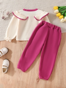 Cute girl's fall set featuring a ruffled waffle top and pink trousers on a cozy rug