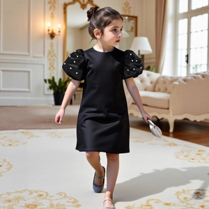 Detail of girl's black satin dress with elegant puff sleeves and white pearl accents