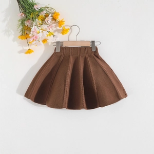 Dettaglio di una gonna a pieghe in maglia marrone per bambina su gruccia in legno