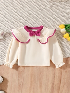Detail of cream long-sleeve toddler top with ruffled collar and bright fuchsia bow