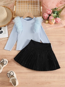 Detail of girl's knit top with mesh ruffles and black pleated skirt with silver glitter