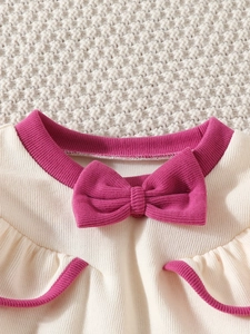 Detail of baby knit set featuring ruffled edges and a pink bow on ivory ribbed fabric