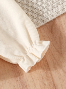 Close-up of cream knit ruffles on sleeve cuff with fine ribbed texture detailing