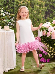 White sleeveless A-line girl's dress with pink 3D floral ruffled hem in a garden setting
