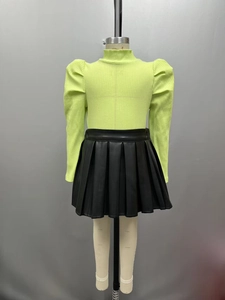 Détail du haut en maille côtelée vert fluo et de la jupe plissée en similicuir noir