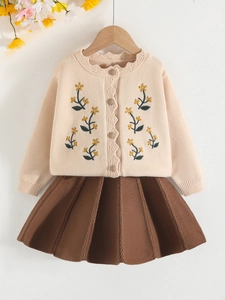 Completo bambina con cardigan beige ricamato e gonna a pieghe marrone su una gruccia