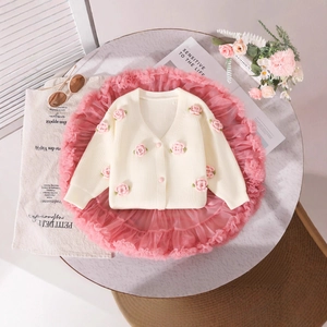 Flat lay of girl's knit cardigan with pink crochet flowers and layered tutu mesh skirt