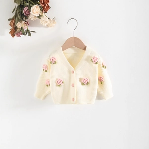 Close-up of cream knit baby cardigan with pink crochet flowers and subtle pink buttons