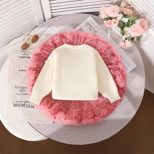 Flat lay detail of girl's cream knit sweater and layered pink tutu tulle skirt
