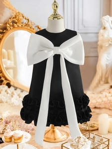 Close-up of elegant black girls' dress featuring a large white bow and layered ruffles