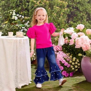 Detail of girls fuchsia ribbed top with pom-poms and flared jeans with pearls