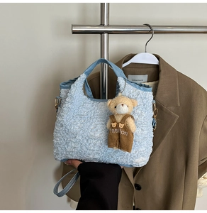 Detailed blue bubble texture tote bag with brown bear pendant on stylish suit background
