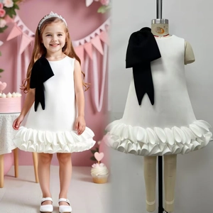 Detail view of white sleeveless dress with large black shoulder bow and layered ruffle hem