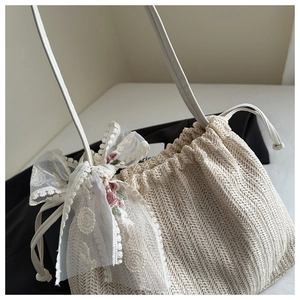 Close-up of woven shoulder bag featuring a floral lace bow and drawstring closure