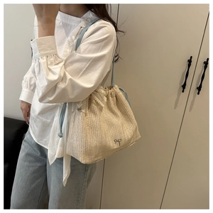 Detail of woven tote bag featuring white lace trim and metal bow charm in beige