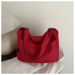 Close-up of bright red nylon tote bag with black adjustable strap and zipper pocket