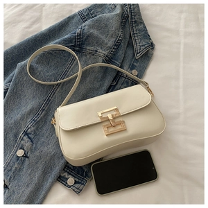 Détail d'un sac bandoulière crème en similicuir avec boucle dorée sur un tissu blanc plissé