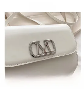 Gros plan sur la boucle métallique en M et la texture fine d'un sac à bandoulière blanc